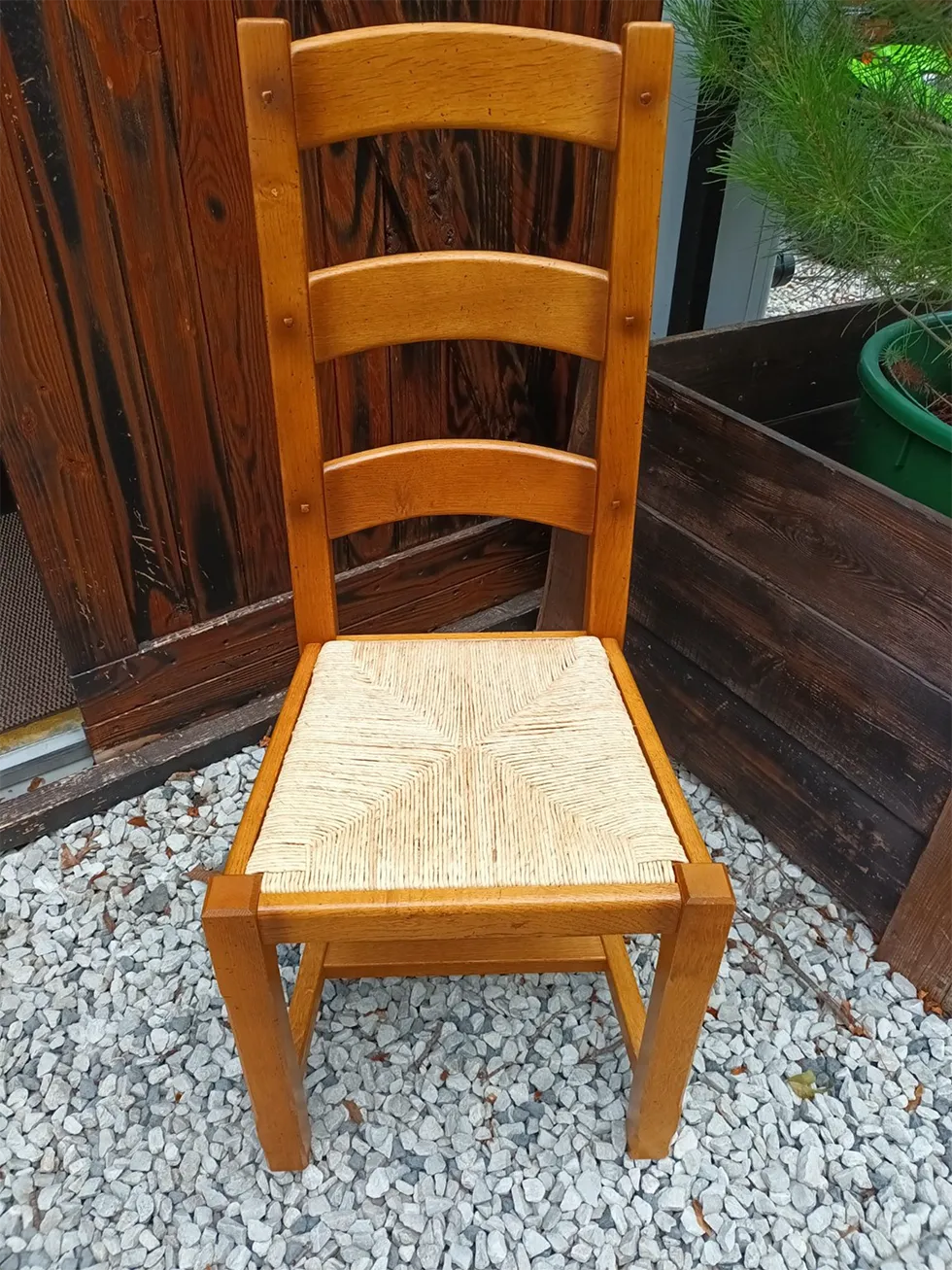 Hellbrauner Holzstuhl mit drei Rückenlehnenstreben und handgeflochtener Sitzfläche aus hellem Naturmaterial.