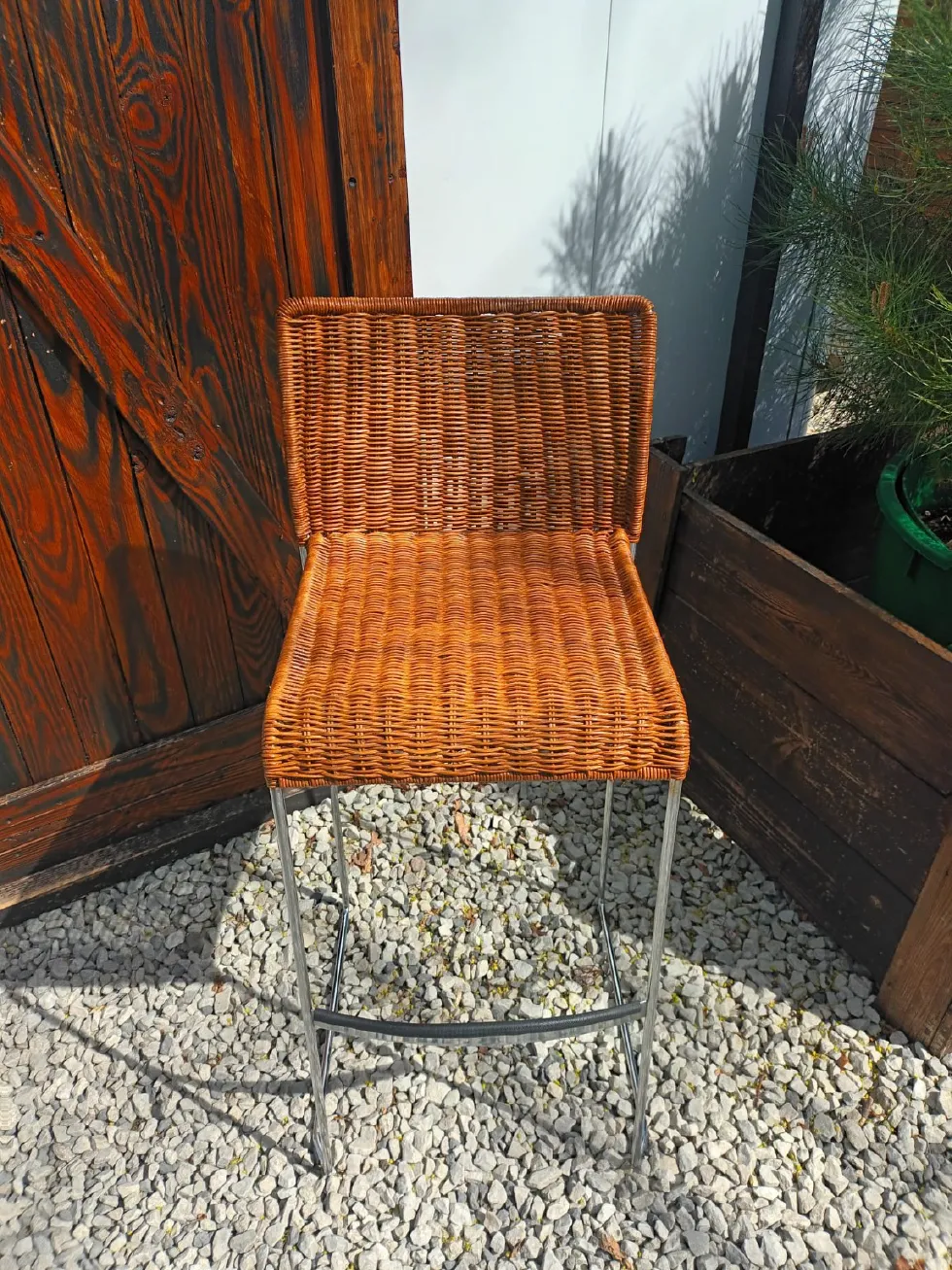 Moderner Barhocker mit silberfarbenem Metallgestell sowie braun lasierter, geflochtener Sitzfläche und Rückenlehne.