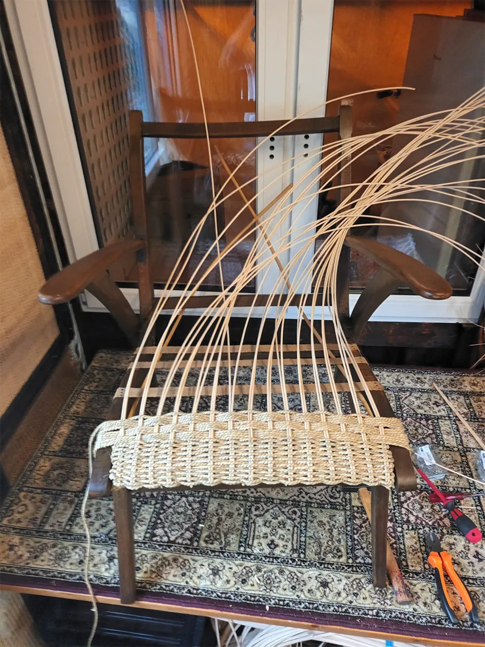 Alter Holzstuhl mit Armlehnen während der handwerklichen Erneuerung seiner Sitzfläche mit hellem Flechtmaterial.