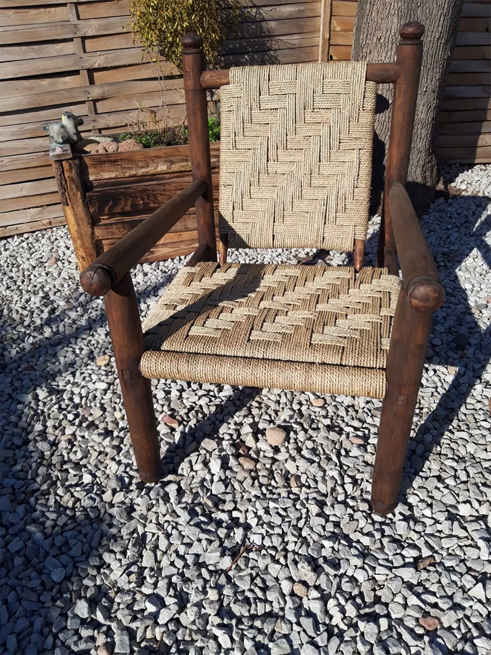 Rustikaler dunkler Holzstuhl mit Armlehnen und hell geflochtener Sitzfläche und Rückenlehne im geometrischen Muster.